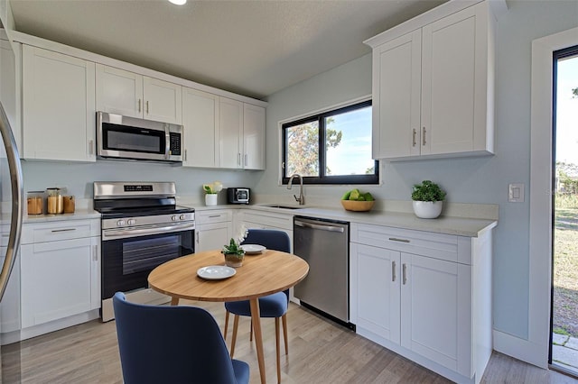 kitchen with appliances with stainless steel finishes, light hardwood / wood-style floors, sink, and white cabinets