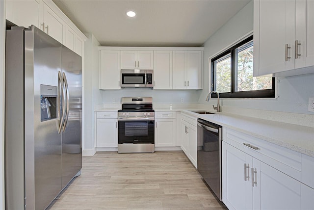 kitchen featuring stainless steel appliances, light countertops, light wood-style floors, white cabinetry, and a sink