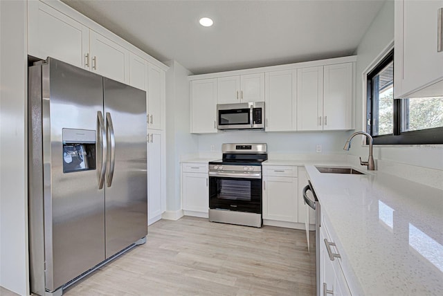 kitchen featuring stainless steel appliances, white cabinets, a sink, and light wood finished floors