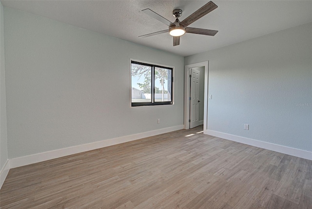 spare room with light wood-type flooring, ceiling fan, a textured ceiling, and baseboards