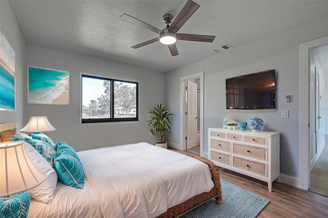 bedroom featuring ceiling fan, ensuite bath, hardwood / wood-style floors, and a textured ceiling