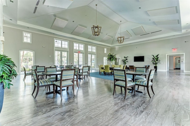 dining area featuring french doors, crown molding, wood-type flooring, a tray ceiling, and a towering ceiling