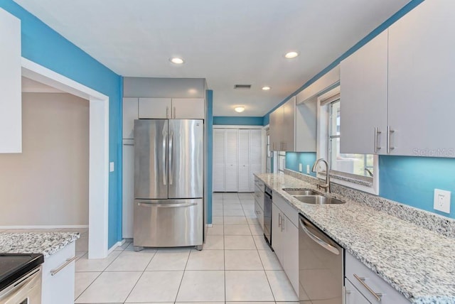 kitchen with stainless steel appliances, sink, light tile patterned floors, and light stone counters