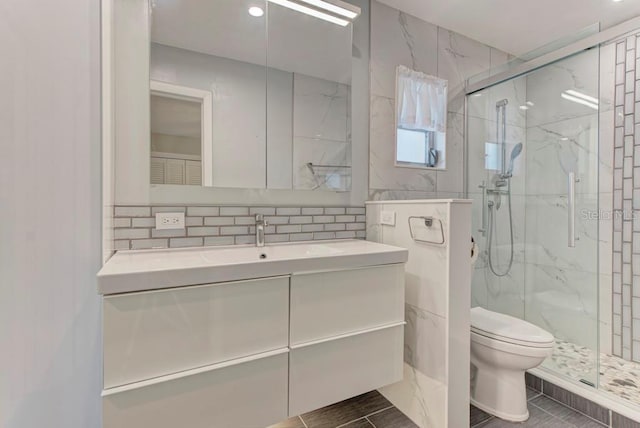 bathroom with toilet, tile walls, vanity, a shower with door, and decorative backsplash