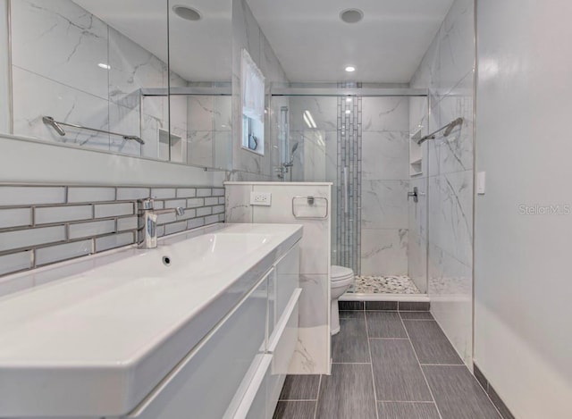 bathroom with vanity, backsplash, a shower with door, and toilet