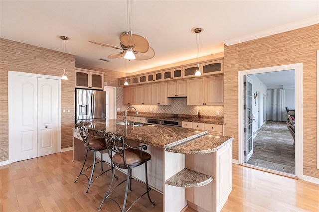 kitchen featuring glass insert cabinets, light wood-style floors, stainless steel refrigerator with ice dispenser, and a kitchen bar