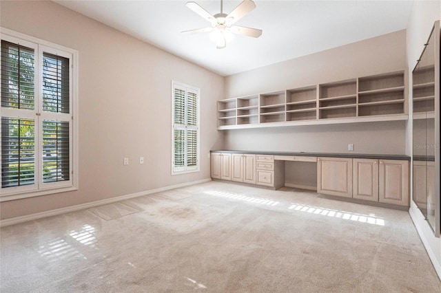 unfurnished office featuring light carpet, built in study area, a ceiling fan, and baseboards