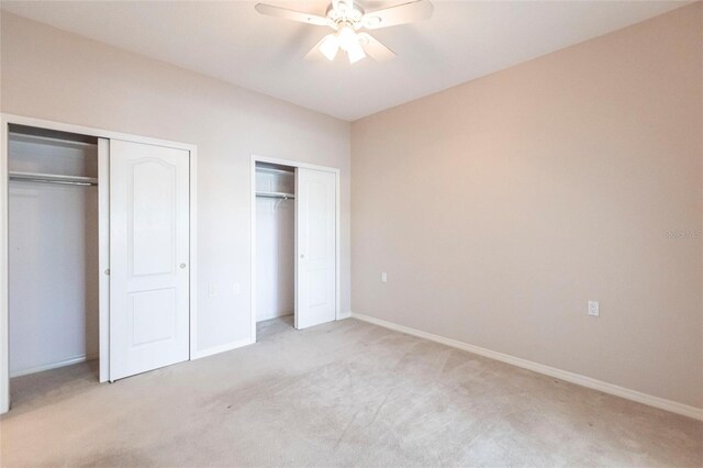 unfurnished bedroom with light carpet, ceiling fan, two closets, and baseboards