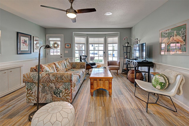 living room with ceiling fan, a textured ceiling, and light hardwood / wood-style flooring