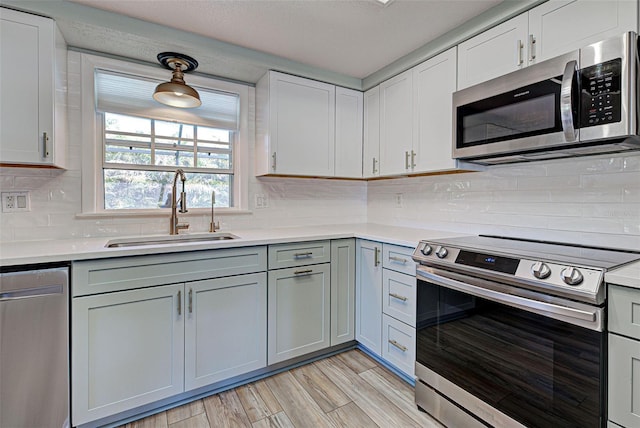 kitchen with appliances with stainless steel finishes, tasteful backsplash, white cabinetry, sink, and light hardwood / wood-style floors