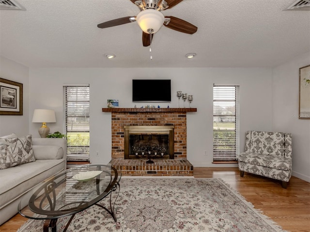 living room featuring ceiling fan, a brick fireplace, hardwood / wood-style floors, and a textured ceiling