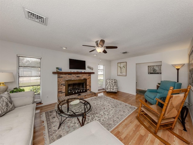 living room with ceiling fan, a fireplace, hardwood / wood-style floors, and a textured ceiling