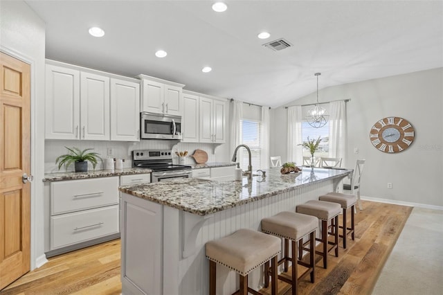 kitchen with light stone countertops, stainless steel appliances, white cabinets, and a center island with sink