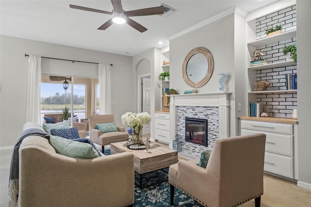 living room with a tile fireplace, ornamental molding, built in features, and ceiling fan