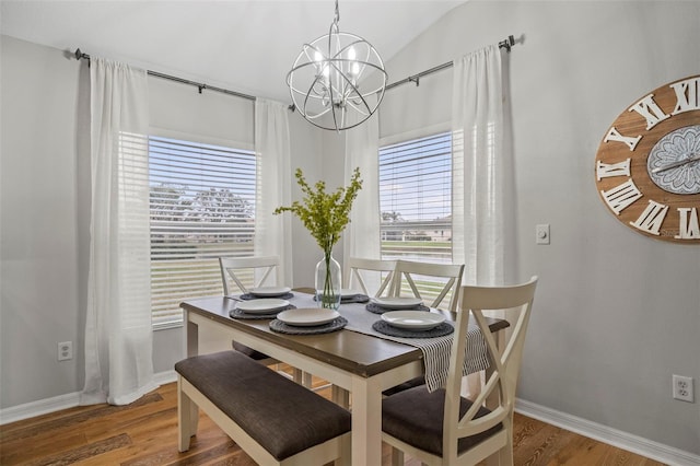 dining space with hardwood / wood-style floors, a notable chandelier, and vaulted ceiling