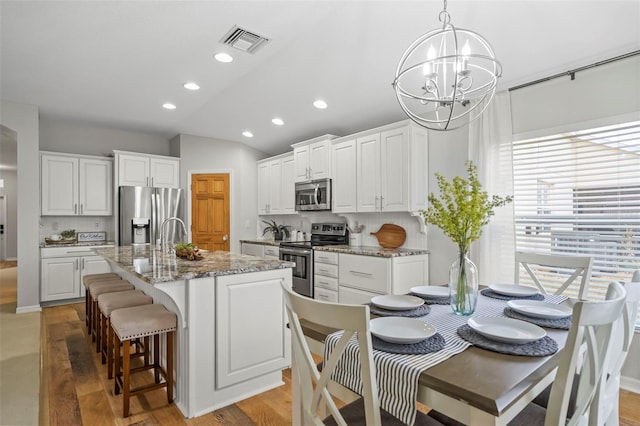 kitchen featuring stone countertops, white cabinetry, a kitchen island with sink, and appliances with stainless steel finishes