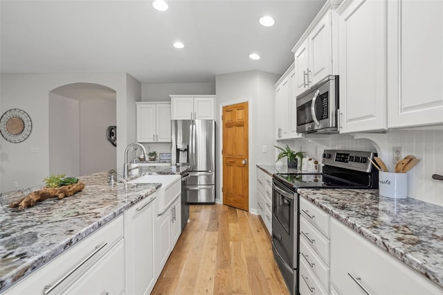 kitchen featuring appliances with stainless steel finishes, light stone countertops, light wood-type flooring, and white cabinets