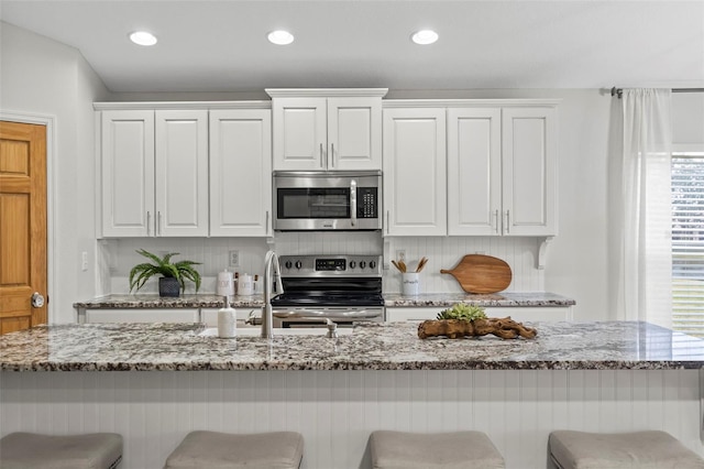 kitchen featuring light stone counters, tasteful backsplash, a kitchen breakfast bar, stainless steel appliances, and white cabinets