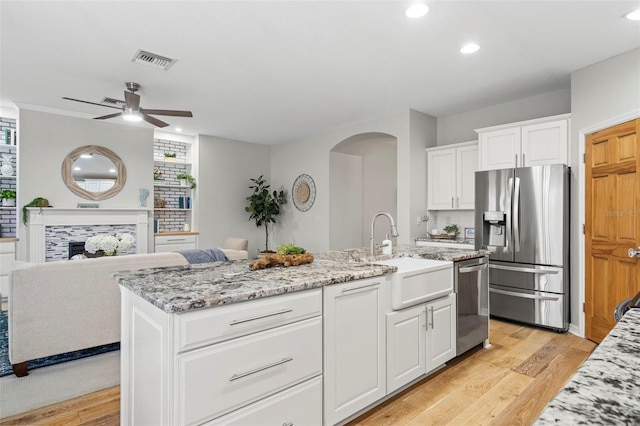 kitchen featuring sink, white cabinetry, a kitchen island with sink, stainless steel appliances, and light stone countertops