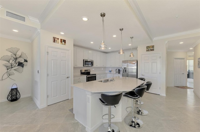 kitchen featuring appliances with stainless steel finishes, sink, white cabinets, hanging light fixtures, and a center island with sink