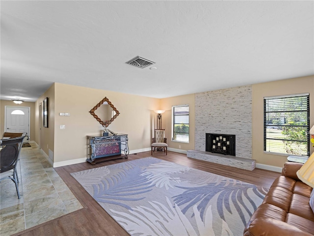 living room with wood-type flooring, a stone fireplace, and a wealth of natural light