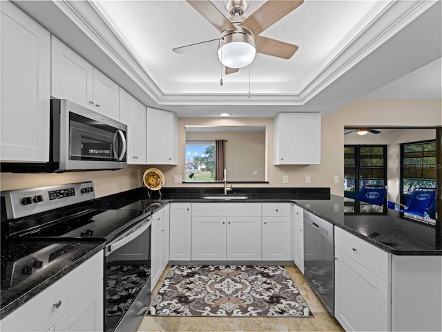 kitchen featuring appliances with stainless steel finishes, white cabinetry, sink, dark stone counters, and a tray ceiling