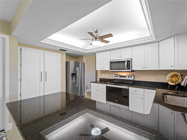 kitchen featuring stainless steel appliances, white cabinetry, dark stone countertops, and a tray ceiling