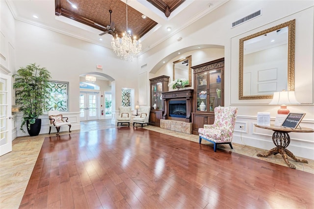 living room featuring crown molding, a towering ceiling, coffered ceiling, wood-type flooring, and french doors