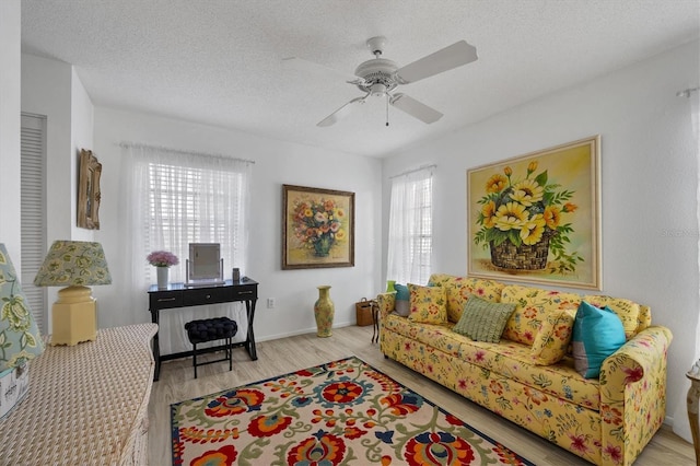 living room featuring ceiling fan, a textured ceiling, and light wood-type flooring