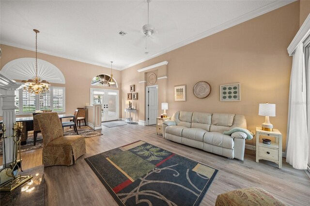 living room featuring french doors, ornamental molding, a notable chandelier, a towering ceiling, and light hardwood / wood-style floors