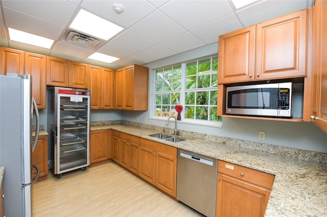 kitchen with sink, appliances with stainless steel finishes, wine cooler, light stone counters, and a drop ceiling