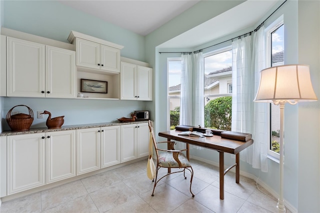 kitchen featuring plenty of natural light, light stone countertops, white cabinetry, and baseboards