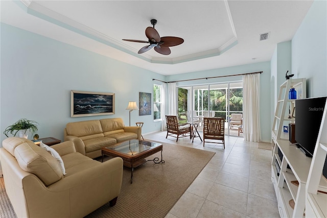 living room with light tile patterned flooring, visible vents, a ceiling fan, ornamental molding, and a tray ceiling