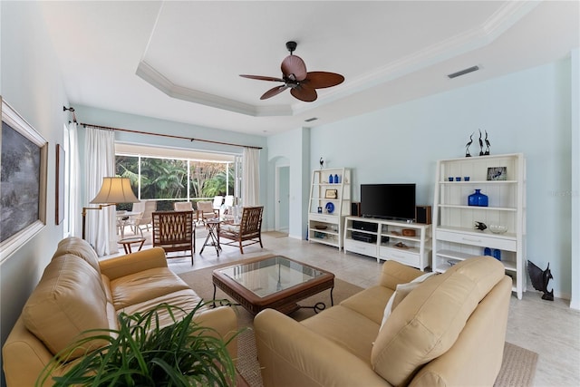 living room with a tray ceiling, arched walkways, visible vents, ornamental molding, and a ceiling fan