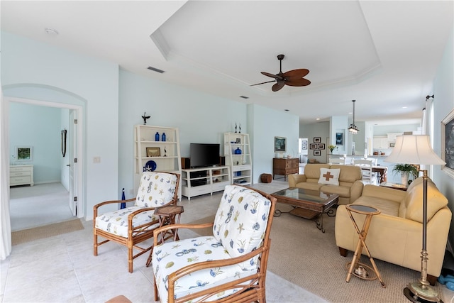 living room featuring light tile patterned floors, visible vents, arched walkways, ceiling fan, and a tray ceiling