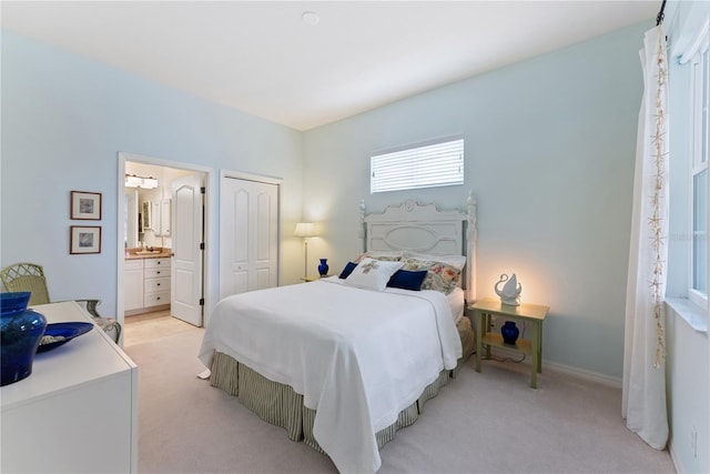 bedroom with baseboards, a closet, connected bathroom, and light colored carpet