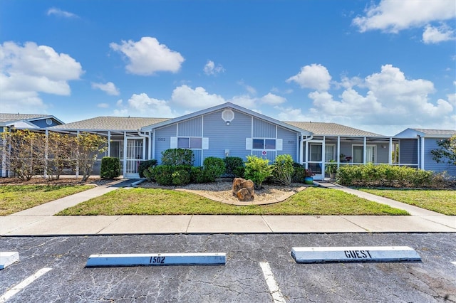 view of front of home with uncovered parking, glass enclosure, and a front yard