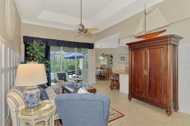 tiled living room featuring a raised ceiling, ornamental molding, and ceiling fan