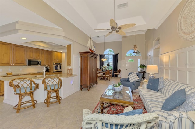 tiled living room with crown molding, ceiling fan, a tray ceiling, and sink