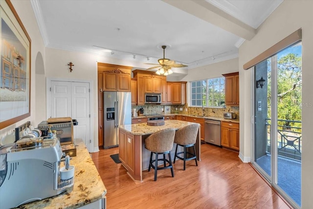 kitchen with a kitchen island, appliances with stainless steel finishes, a kitchen breakfast bar, light stone counters, and light hardwood / wood-style floors