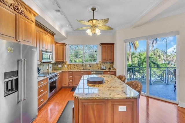 kitchen with tasteful backsplash, light wood-type flooring, ornamental molding, a kitchen island, and stainless steel appliances