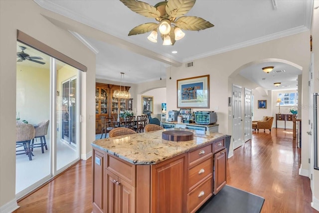 kitchen featuring pendant lighting, ceiling fan, ornamental molding, light hardwood / wood-style floors, and a kitchen island