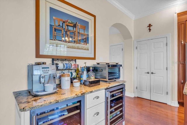 bar featuring ornamental molding, beverage cooler, light stone countertops, and hardwood / wood-style floors