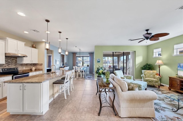 kitchen featuring sink, a breakfast bar area, stainless steel electric range oven, hanging light fixtures, and a center island with sink