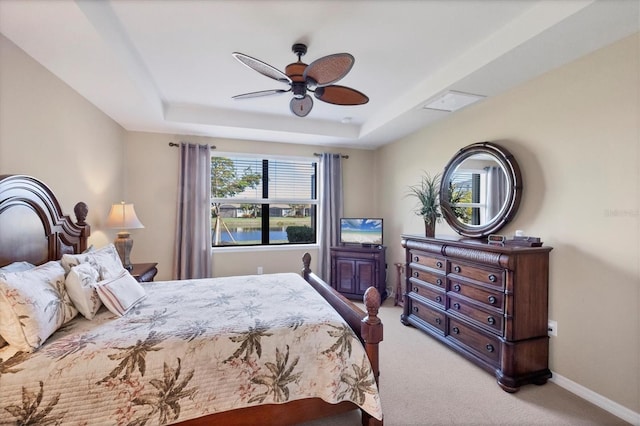 carpeted bedroom with a raised ceiling and ceiling fan