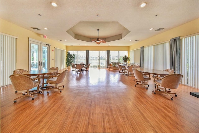 interior space with french doors, a raised ceiling, a textured ceiling, and light wood-type flooring