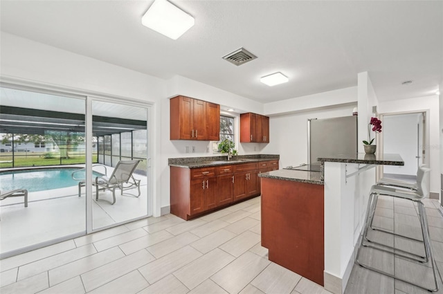 kitchen featuring stainless steel refrigerator, a kitchen breakfast bar, a center island, black electric cooktop, and dark stone counters