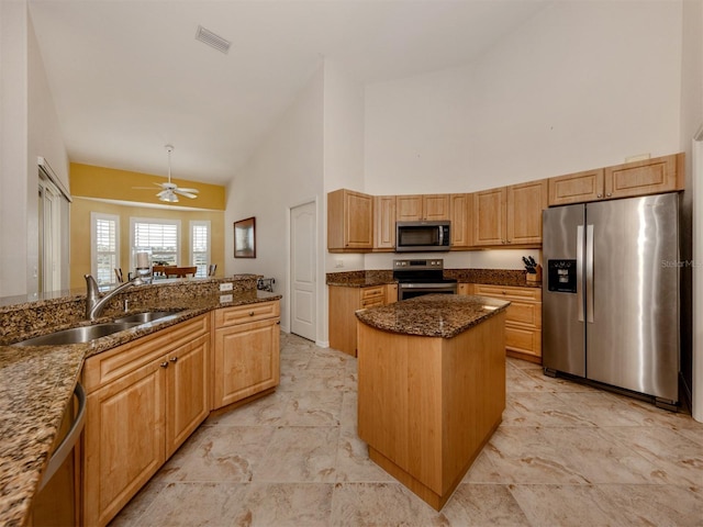 kitchen featuring sink, stainless steel appliances, a center island, and dark stone counters