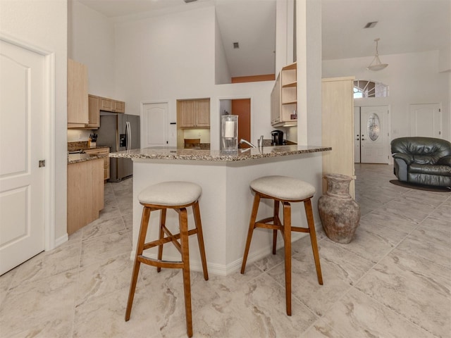 kitchen featuring stainless steel refrigerator with ice dispenser, a kitchen bar, light stone counters, kitchen peninsula, and a towering ceiling