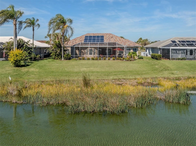 rear view of property with a lawn, a water view, solar panels, and glass enclosure